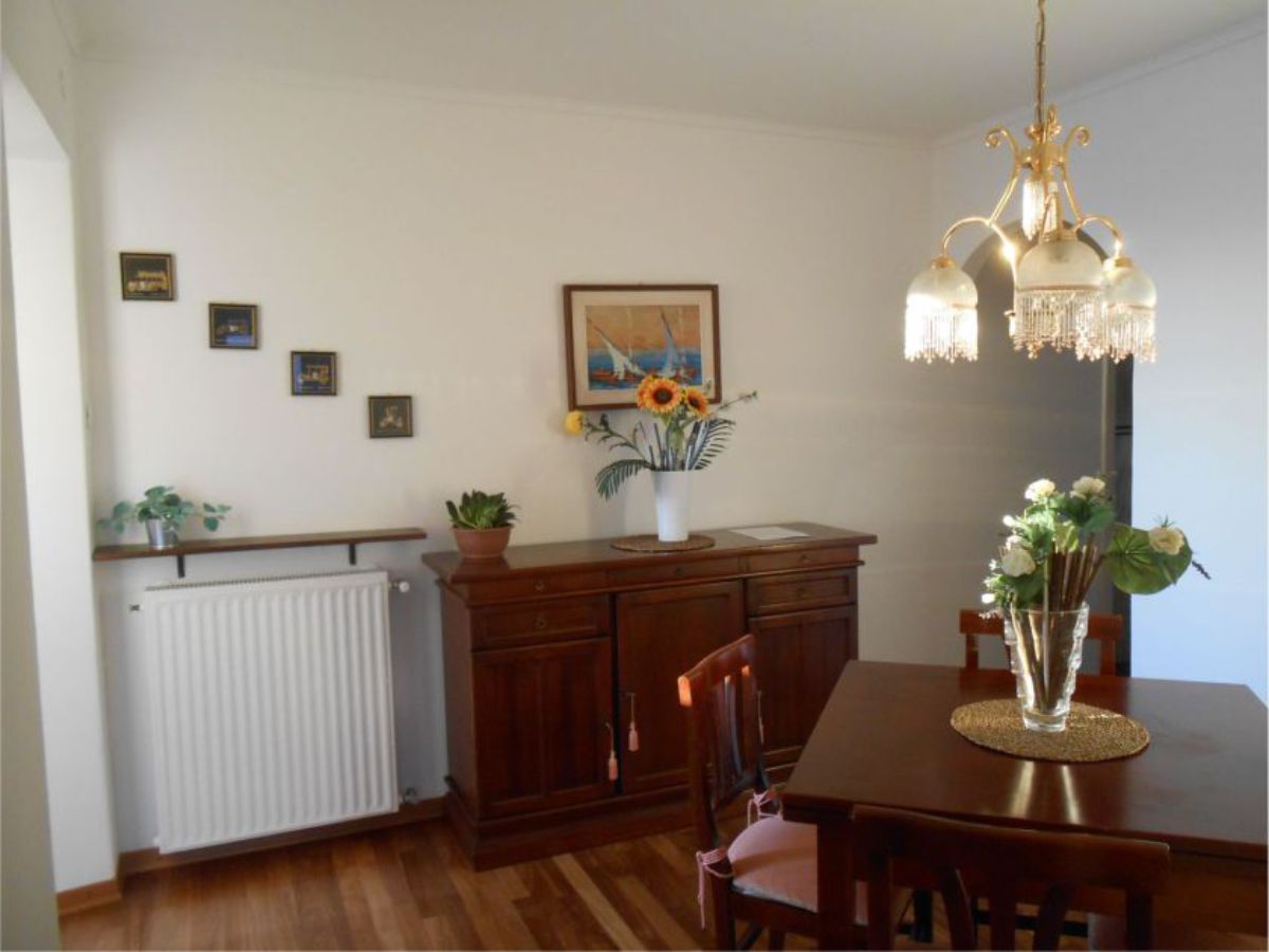 table with a vase of flowers and chairs, chest of drawers with a vase of flowers, radiator, pictures on the wall, wall lamp